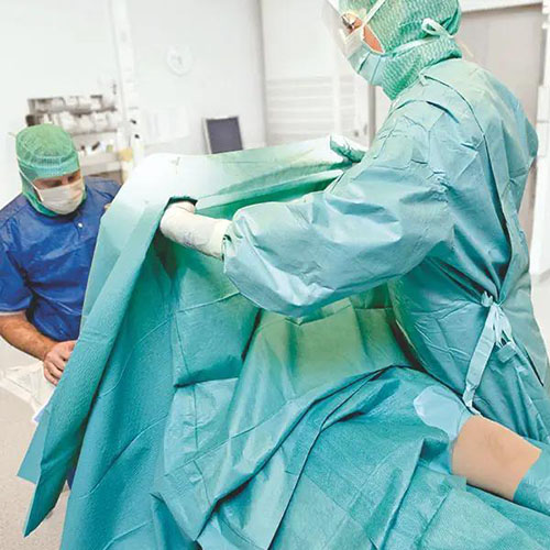 Medizinisches Personal in OP-Kleidung legt ein grünes steriles Abdecktuch mit einer Öffnung über einen Patienten